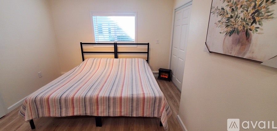 A bed with a striped comforter is in a room with a window and a painting on the wall.