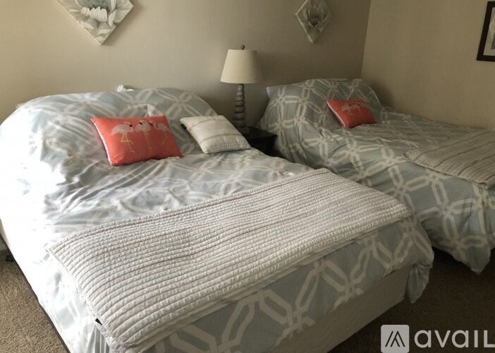 Two beds with grey and white bedspreads and red pillows.