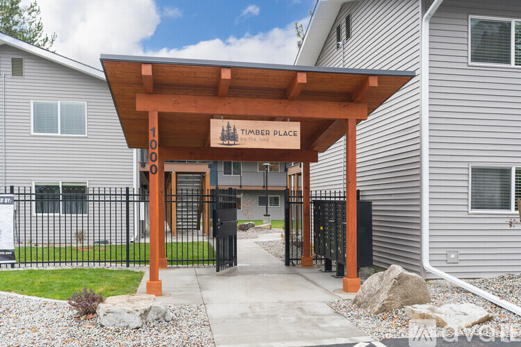 A timber place sign is on a wooden structure in front of a building.
