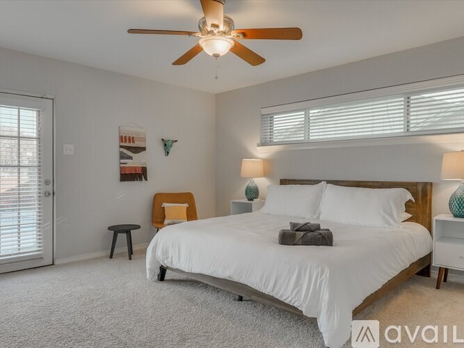 A bedroom with a large bed, a ceiling fan, and a nightstand with a lamp.