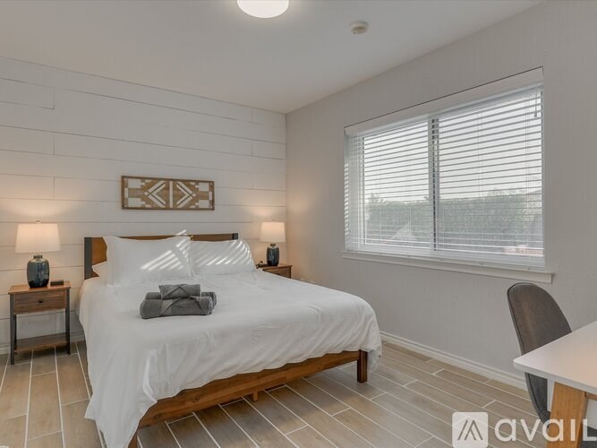 A bedroom with a large bed, a nightstand with a lamp, and a window with blinds.