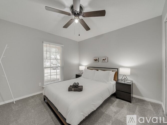 A bedroom with a large bed, a ceiling fan, and a window with blinds.