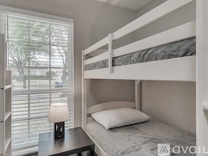 A white bunk bed with a table and a lamp on it.