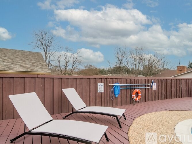 Two white chairs on a wooden deck with a lifebuoy and a blue towel hanging on a railing.