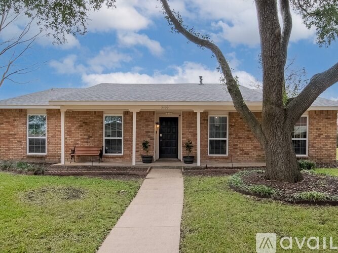 A brick house with a tree in front and a walkway leading to the door.