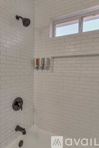 A white tiled bathroom with a window and a shower.