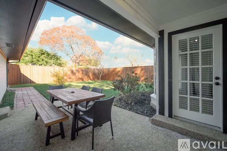 A patio with a table and chairs is shown with a view of a tree and a fence.