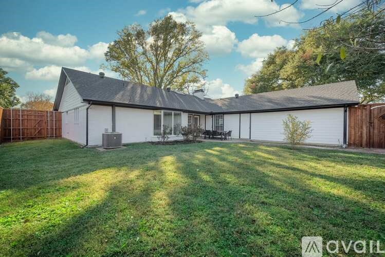 A house with a white exterior and a grey roof is surrounded by a green lawn.