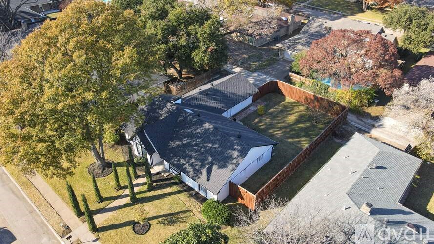 A house with a grey roof and a brown fence is surrounded by trees.