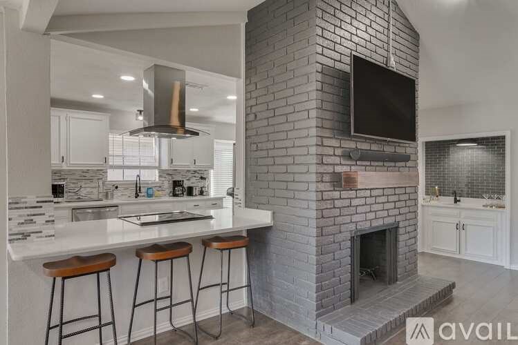 A modern kitchen with a brick fireplace and bar stools.