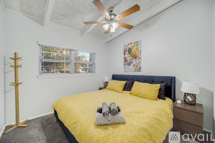 A bedroom with a yellow bedspread and a ceiling fan.