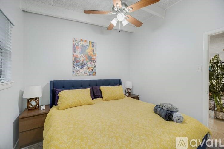 A bedroom with a bed, pillows, a ceiling fan, and a painting on the wall.