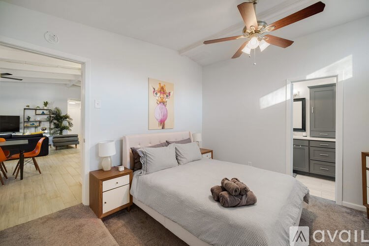 A bedroom with a bed, a ceiling fan, and a painting on the wall.