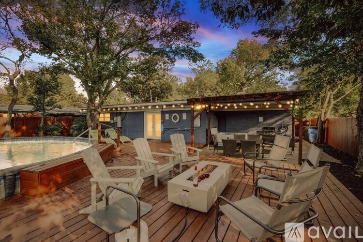 A wooden deck with chairs and a hot tub is surrounded by trees.
