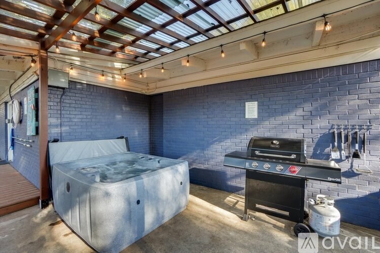 A hot tub is in the middle of a room with a brick wall and a barbecue grill.