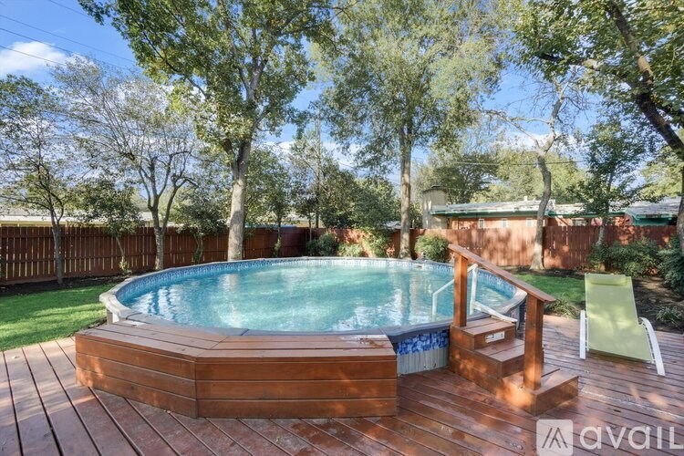 A wooden deck with a round blue pool in the middle surrounded by trees.
