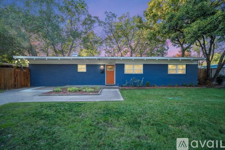 A blue house with a brown door and windows is surrounded by greenery.