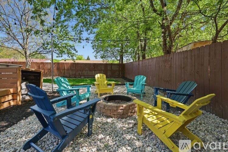 A set of four brightly colored Adirondack chairs are arranged around a fire pit in a backyard.