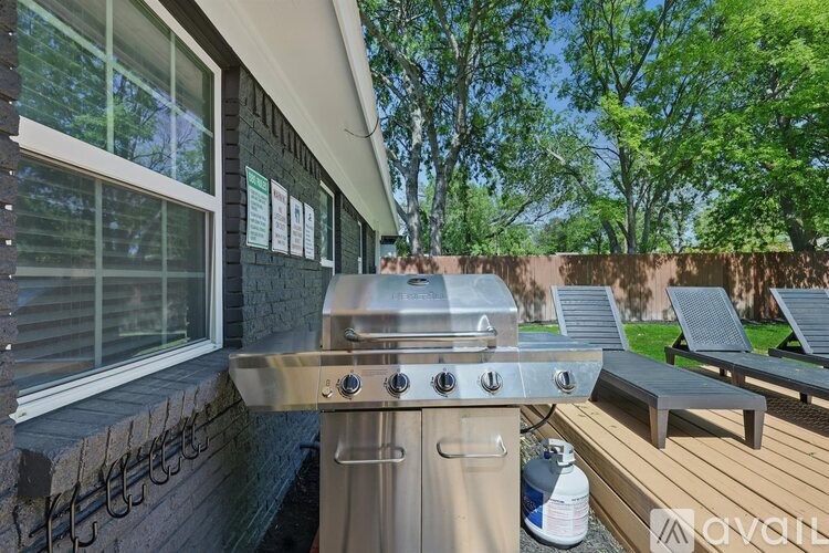 A stainless steel grill is on a wooden deck outside a house.