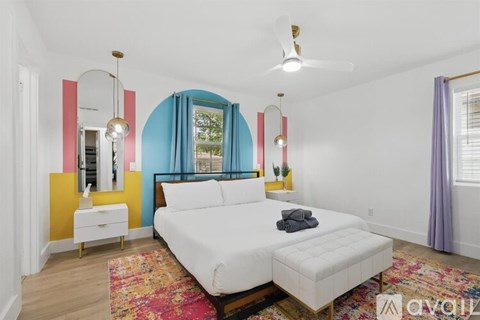 A bedroom with a white bed and a colorful accent wall.
