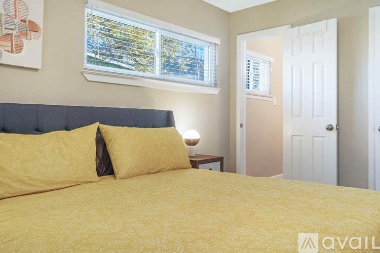 A bedroom with a bed, two pillows, a nightstand, and a window with blinds.
