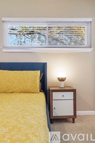 A bedroom with a bed, a nightstand, and a window with blinds.