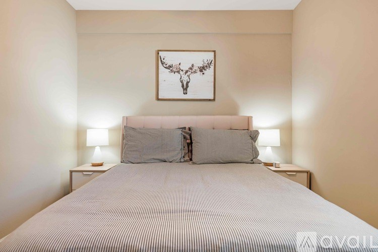 A bedroom with a bed, two lamps, and a framed piece of artwork on the wall.