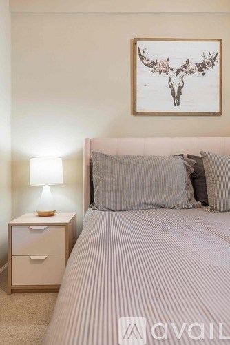 A bedroom with a bed, nightstand, and a deer head picture on the wall.