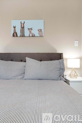A bed with a striped comforter and two pillows sits under a picture of three deer heads.