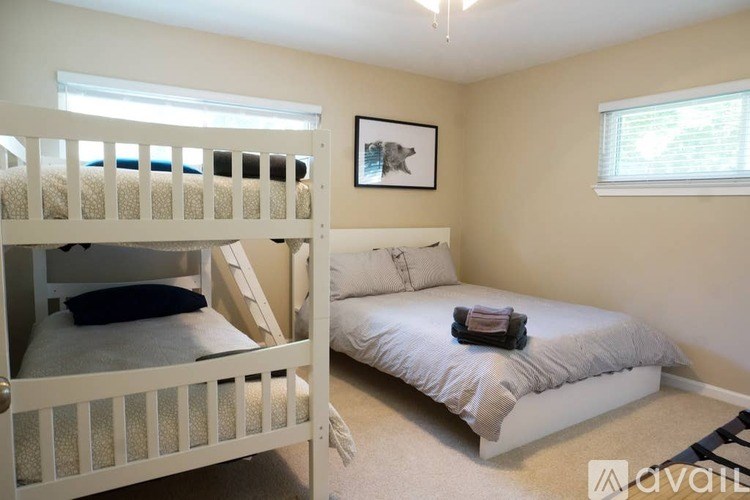 A bedroom with a white bunk bed and a white bed with pillows.