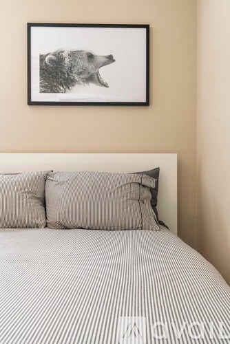 A bed with a striped comforter and two pillows with a picture of a bear on the wall above it.