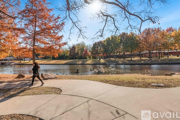 A person is walking on a paved path near a pond with trees in the background.