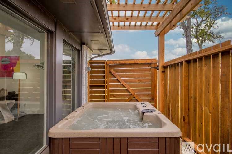 A hot tub is on a patio with a wooden deck and a pergola.