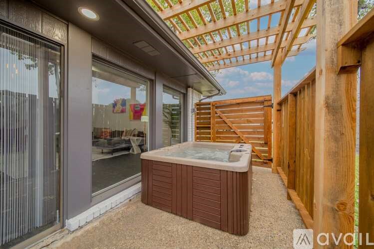 A hot tub is on a patio with a wooden pergola above it.