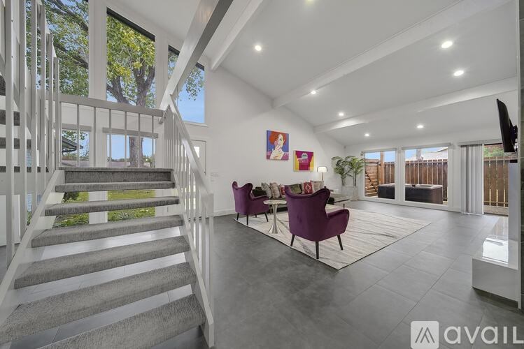 A spacious living room with a staircase on the left and a television on the right.