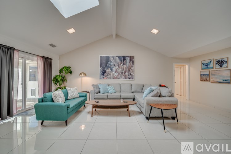 A spacious living room with a skylight, a green sofa, a wooden coffee table, and a large painting on the wall.