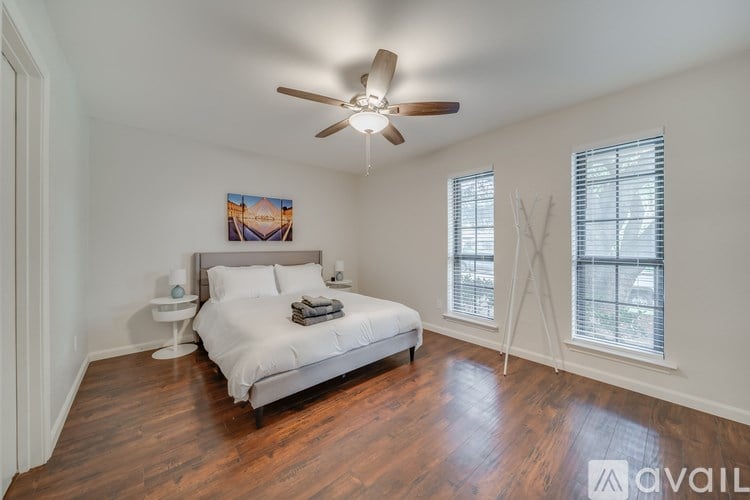 A bedroom with a bed, a ceiling fan, and a painting on the wall.