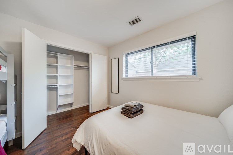 A bedroom with a white bed and a window with blinds.