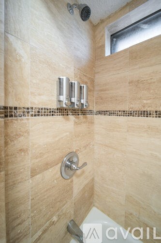 A bathroom with beige tiles and a shower head.
