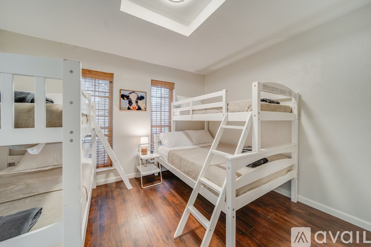 A bedroom with white walls and wooden floors has two bunk beds and a small table.
