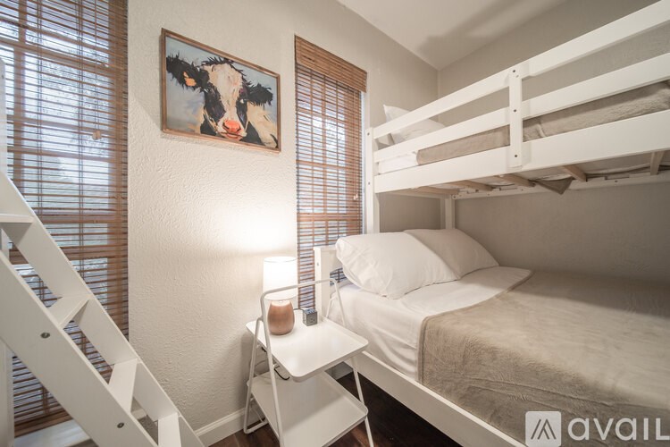 A white bunk bed with a white chair and a painting of a cow on the wall.