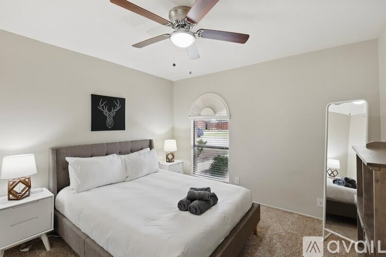 A bedroom with a bed, a ceiling fan, and a window with a view of the street.