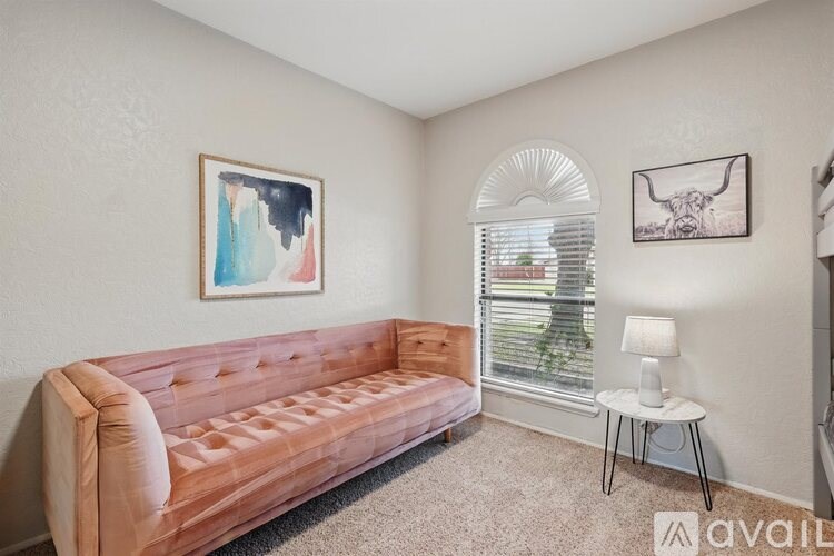 A living room with a couch, a painting, a window with blinds, a lamp, and a small table.