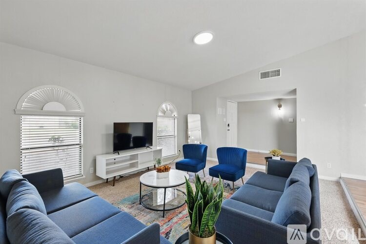 A living room with a grey sofa, a white coffee table, a TV, and a window with blinds.