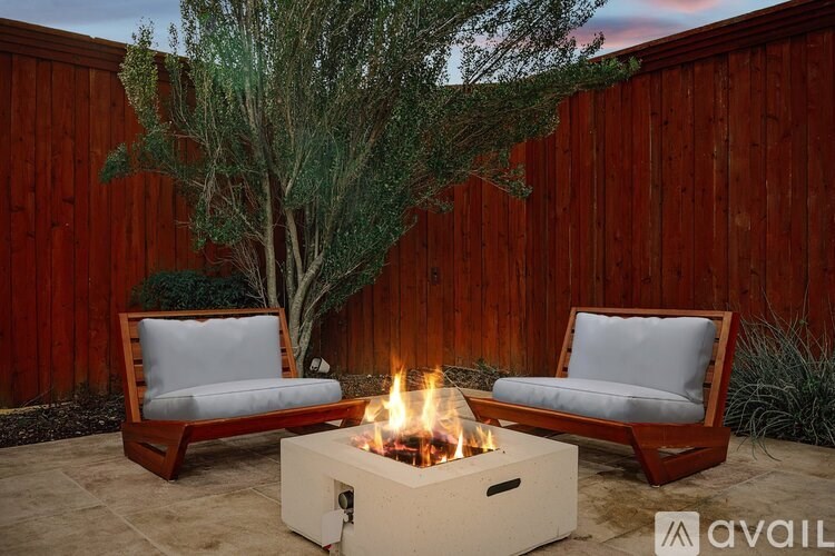 A fire pit with two chairs and a tree in the background.