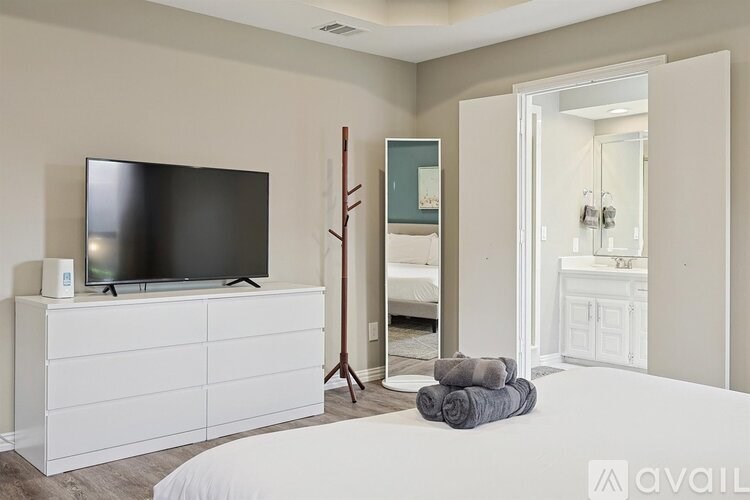 A bedroom with a white bed, a white dresser, and a black television.