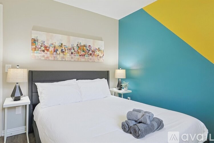 A bedroom with a white bed and a painting above it.