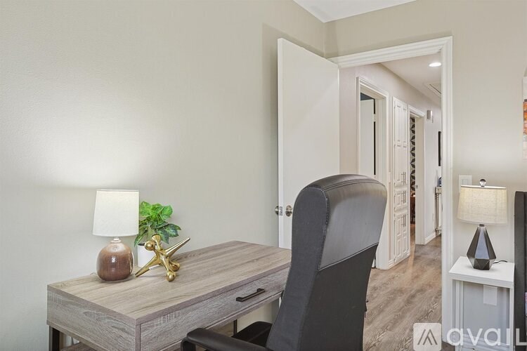 A desk with a chair and a lamp is in the foreground of a room.