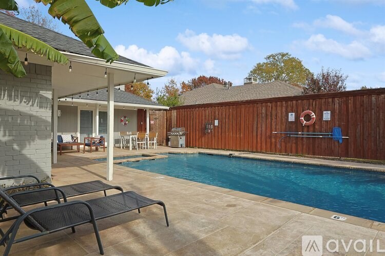 A pool with a black lounge chair and a white table in front of a house.