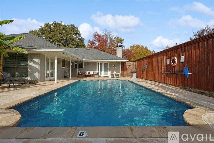 A pool in a backyard with a house and trees in the background.